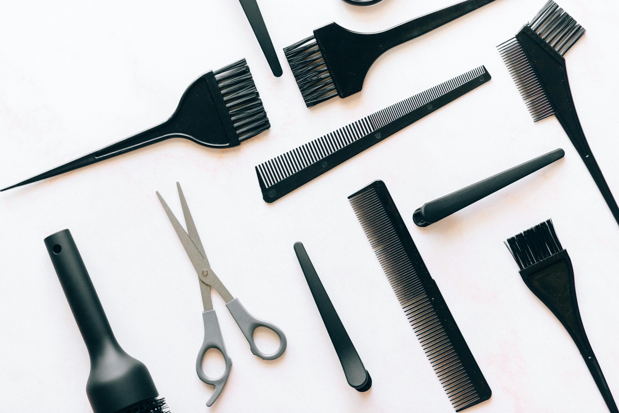 Flat lay of essential hairdressing tools including brushes, combs, and scissors on white background.